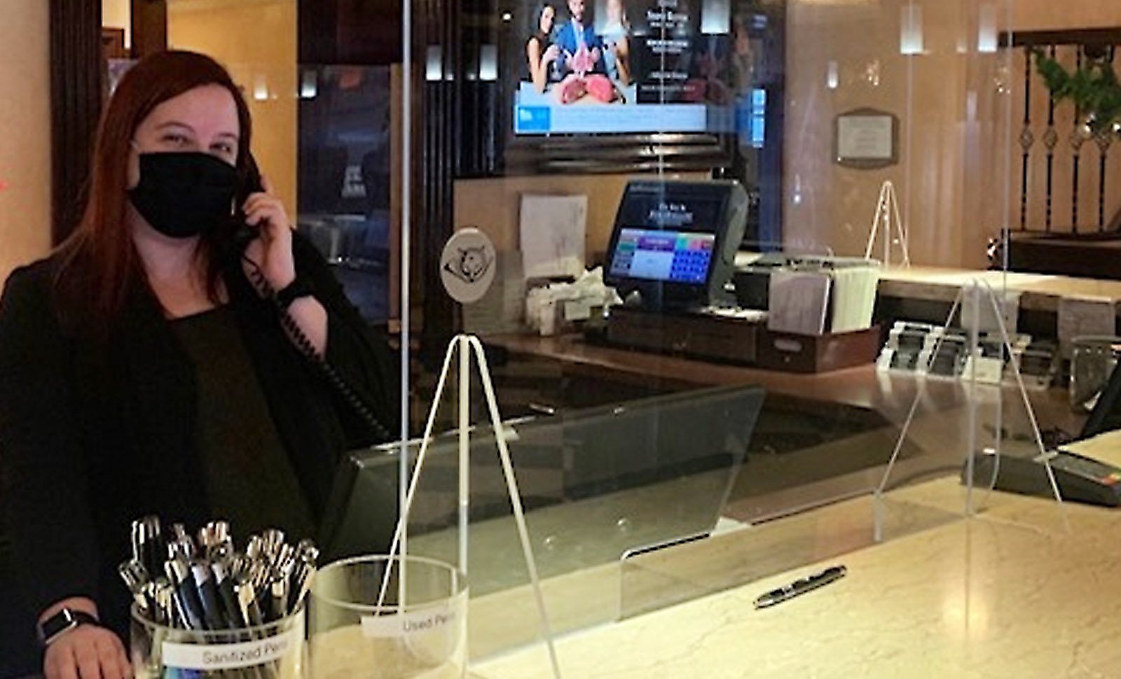 mask-wearing woman behind the hotel front desk smiling at the camera